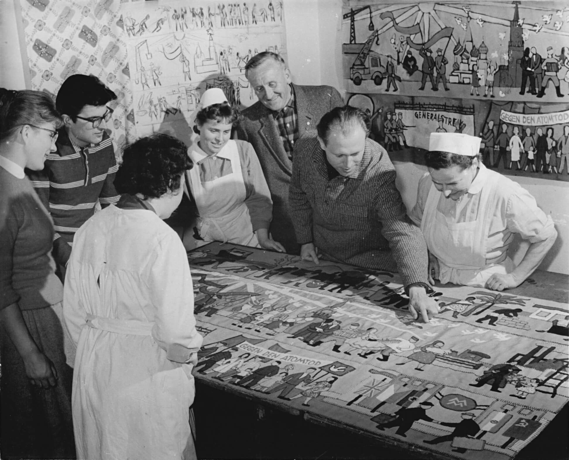 Zur Vorbereitung der III. Arbeiterfestspiele 1961. An den III. Arbeiterfestspielen 1961, die in Magdeburg stattfinden, beteiligt sich der Zirkel "Bildnerisches Volksschaffen" des Krankenhauses Altscherbitz, Kreis Leipzig, mit einem Applikations-Wandbehang "Der Sozialismus siegt". Der Wandbehang wird von 5 verschiedenen Gewerkschaftsgruppen zur Auszeichnung mit dem "Kunstpreis des FDGB" vorgeschlagen. UBz: Der Leiter des Zirkels, Heinz Mutterlose, Mitglieder des Zirkels und Angestellte des Krankenhauses begutachteten zum letzten Mal den Wandbehang, bevor er nach Magdeburg geschickt wird. Quelle: BArch, Bild 183-81069-0001.